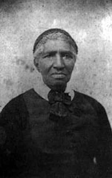 A grainy, black and white photograph shows an older Black woman, Clara Brown, looking straight ahead. She wears a dark dress with a high collar and a large bow at the neck, and her hair is pulled back, revealing gray or white at the temples.
