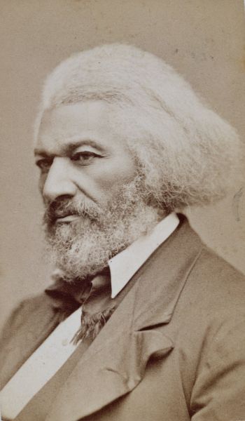 A sepia-toned portrait shows a man with a full, white beard and voluminous, grey-white hair. He is turned three-quarters, wearing a dark coat and a white-collared shirt.
