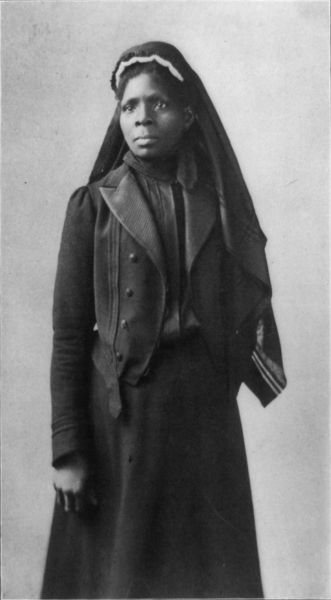 A black-and-white portrait shows Susie King Taylor looking slightly to the left of the camera. She wears a long-sleeved dark jacket over a dark dress, and a dark veil with a light-colored headband.