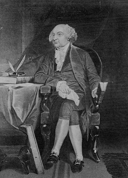 A black and white engraving depicts John Adams seated in an upholstered armchair with his legs crossed, facing slightly to the left. He wears a colonial-era coat, waistcoat, breeches, and stockings, resting his right arm on a table that holds books and quill pens. 