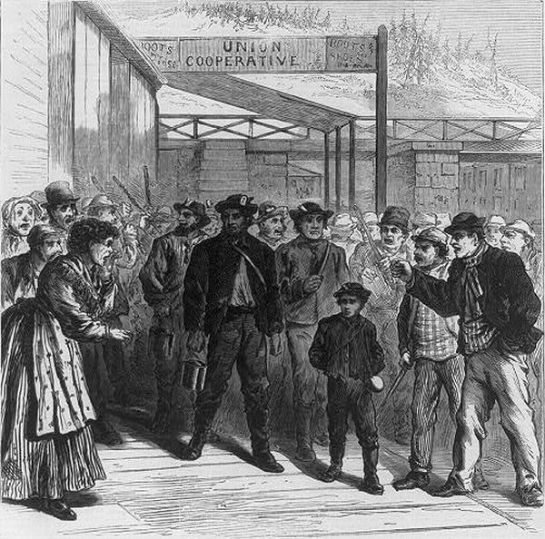 An illustration shows a tense confrontation between a group of striking workers and a man accompanied by a young boy in front of a building labeled 