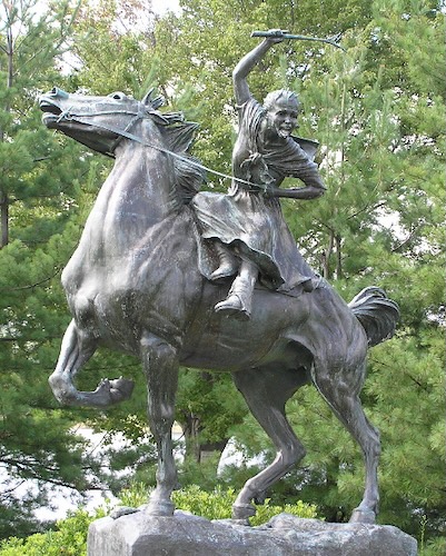 A bronze statue shows a young woman on a rearing horse, brandishing a stick or weapon over her head. Her face has an intense expression, and she is wearing a dress with her hair tied back.