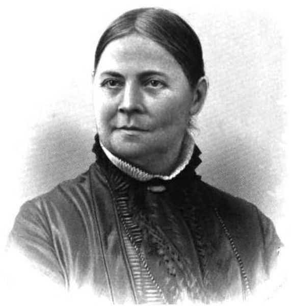 This black and white portrait shows Lucy Stone from the chest up, facing slightly to the left with a calm expression. She is wearing a dark, high-collared dress with ruffled detailing and a small white lace trim around the neck.