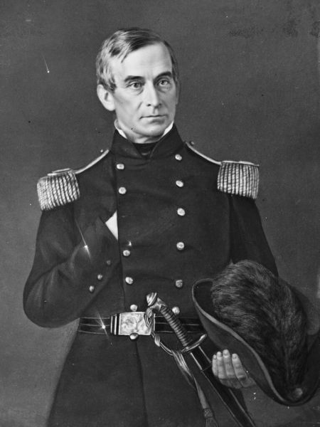 A black and white portrait shows Major Robert Anderson in a formal U.S. Army officer's uniform, featuring a double-breasted coat with large epaulettes. He stands with his right hand tucked into his coat in a Napoleonic pose while his left hand holds a dress hat and rests near a ceremonial sword at his waist.